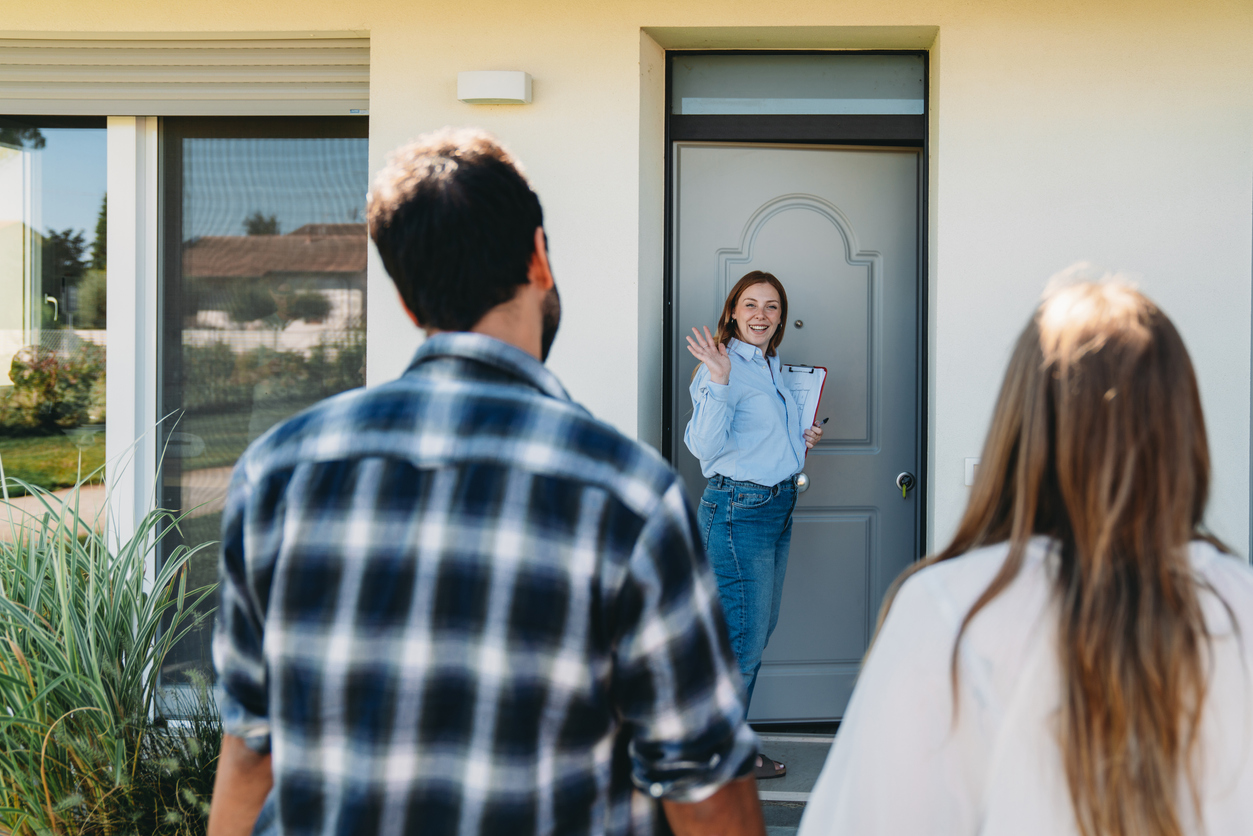A real estate agent is showing an house to a couple at the entrance of the home